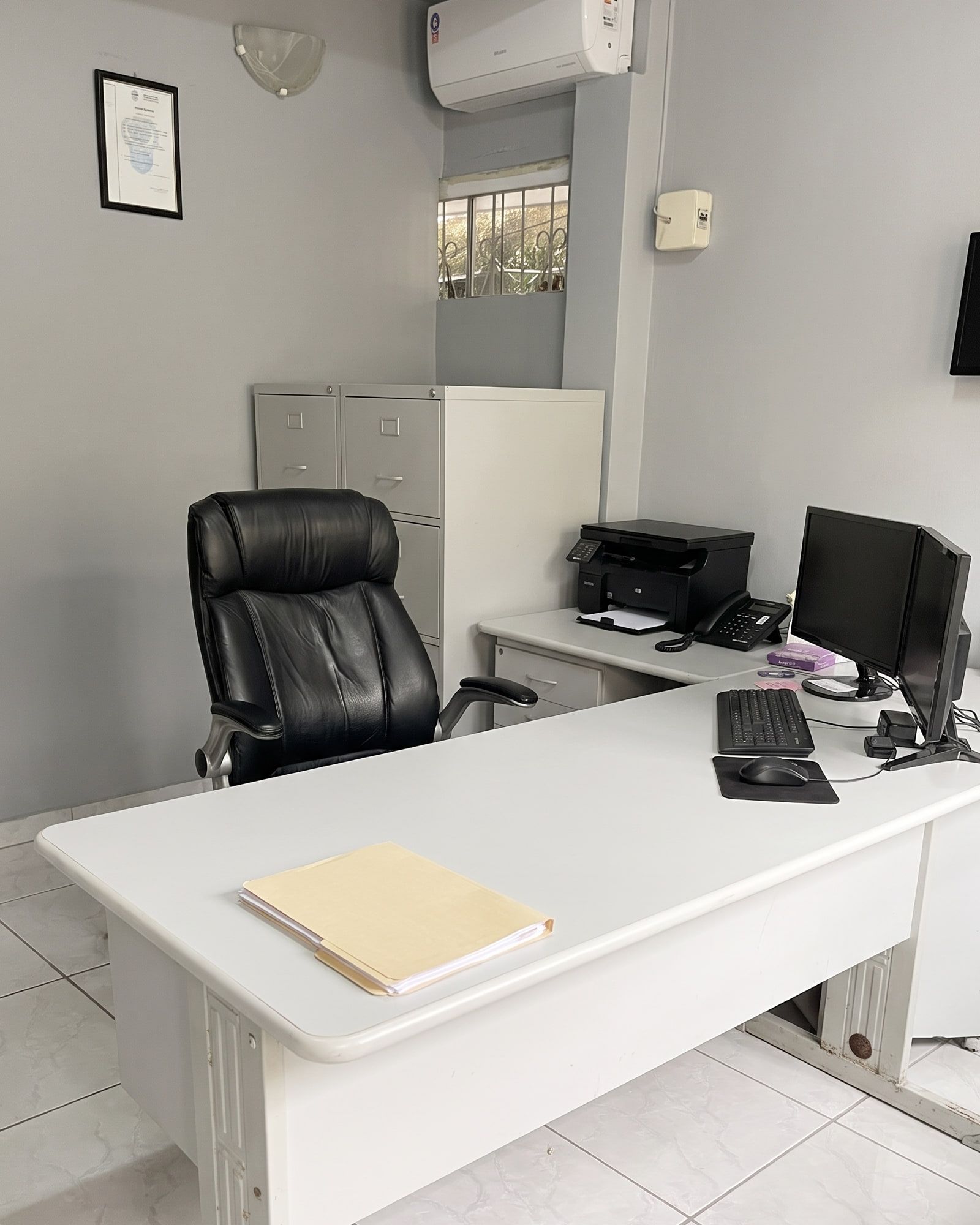 Mesa de atendimento do escritório da Nepack, com cadeira executiva, impressora e um certificado emoldurado na parede